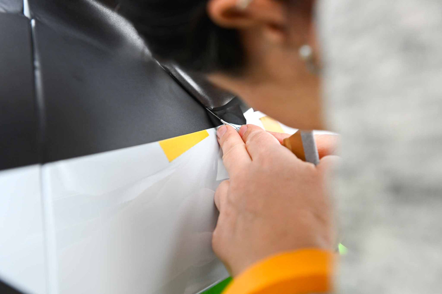 Eine Werbetechnikerin schneidet präzise eine Folie bei einer Fahrzeugbeschriftung